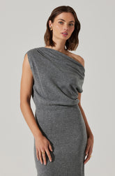A woman is wearing a sleeveless, one-shoulder gray knit dress with a draped top that has a relaxed fit and a fitted skirt. She accessorizes with gold earrings and rings.